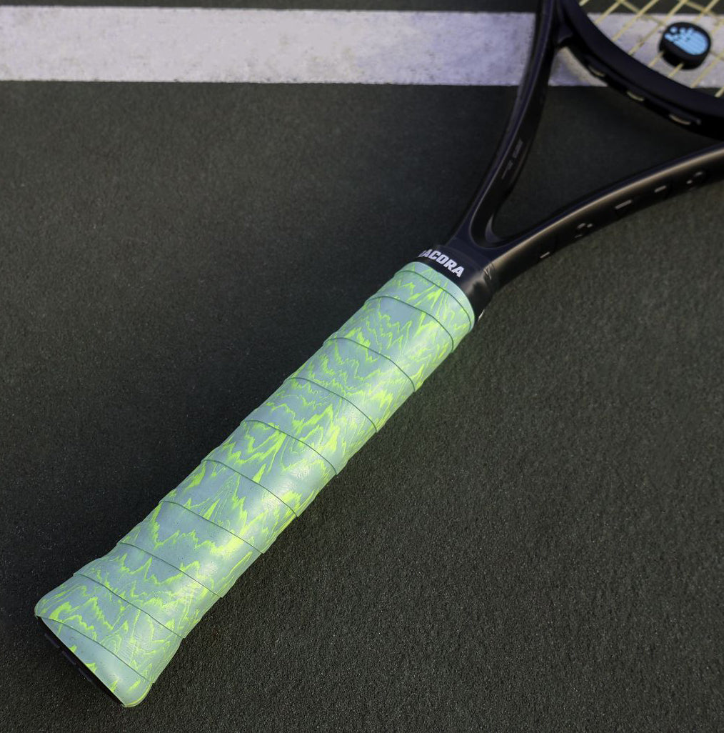 Green waves tennis overgrip on tennis racket lying on tennis court.