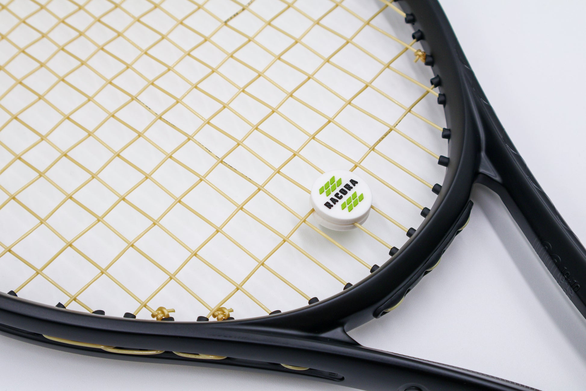 Racora white vibration dampener on tennis racket shown at an angle